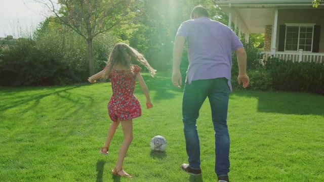 Slow motion tracking shot of father and daughter playing soccer in yard / Pleasant Grove, Utah, United States