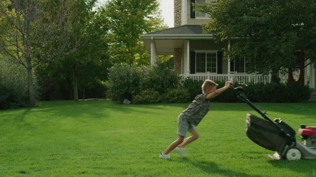 Boy pushing lawnmower on lawn near house / Pleasant Grove, Utah, United States