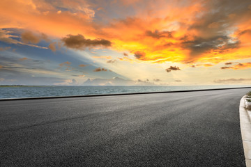 Naklejka premium Droga asfaltowa i dramatyczne niebo z wybrzeżem o zachodzie słońca