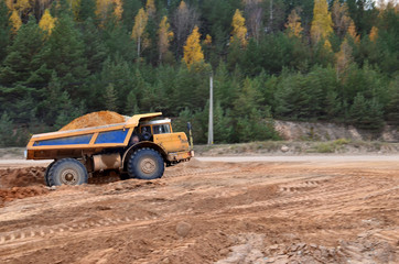 Obraz premium Earth mover loading dumper truck with sand in quarry. Excavator loading sand into dumper truck.Quarry for the extraction of minerals. Large quarry dump truck. Production useful minerals.