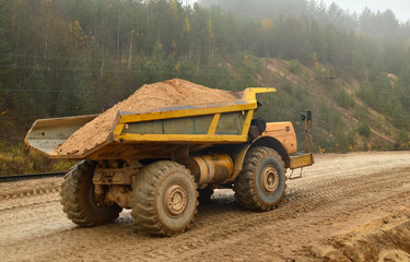 Obraz premium Earth mover loading dumper truck with sand in quarry. Excavator loading sand into dumper truck.Quarry for the extraction of minerals. Large quarry dump truck. Production useful minerals.