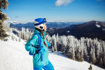 Fototapeta na wymiar A beautiful girl in winter clothes, a blue helmet and a green jacket is having a great time in the mountains. Concept of travel, leisure, freedom, sport. Beautiful nature, places, great weather.