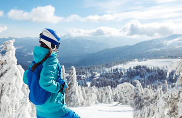 Fototapeta na wymiar A beautiful girl in winter clothes, a blue helmet and a green jacket is having a great time in the mountains. Concept of travel, leisure, freedom, sport. Beautiful nature, places, great weather.
