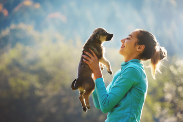young woman is playing with a cute little puppy on a green grass in the campsite