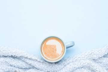 A cup of coffee with cream and a warm blanket. Cool background. Soft light. Top view