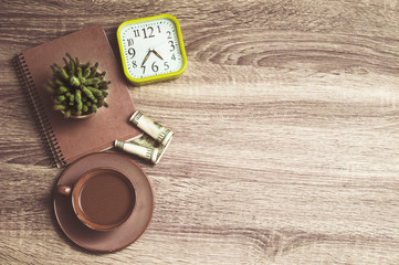 Clock, notebook, cactus, money and a cup of coffee on a wooden background. Top view