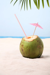 Coconut with straw and drink umbrella on white sand