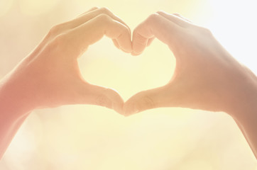 Fototapeta premium Kobiece ręce kształt serca na natura słońce pochodni i rozmycie streszczenie tło liść.