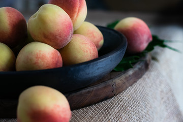 Fresh peaches fruits with in black plate on dark wooden rustic background, angle view
