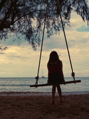 Girl on a swing is looking at the sea.