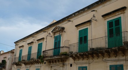 Fototapeta na wymiar City of Noto. Province of Syracuse, Sicily. Perspective of a house with balconies and all its windows painted of green.