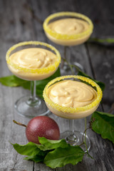Passion fruit mousse in three small glasses on dark wooden background, vertical composition