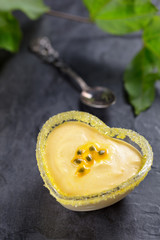 Passion fruit mousse in heart shaped glass ramekin on dark background, top view, vertical composition
