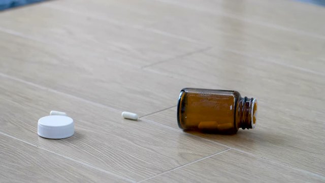 Slow motion of glass bottle filled with capsule pills falling to the wooden floor at home, Spilling the medicine