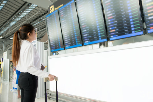 Asian young woman in international airport looking at the flight information board, checking her flight in airport.