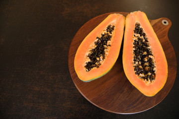 Organic two half papaya with seeds on a brown wooden plate on a brown background. Top view. Flat lay. With copy space for text or image.
