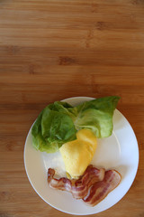 fried bacon with eggs with green leaves of lettuce on a white plate on a wooden background. With copy space for text. Flat lay. Top view.	