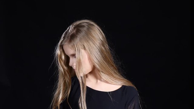 Model girl posing on black background. Blond longhaired teenager looking at camera showing face emotion. 4k
