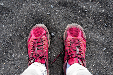 Flat top lay closeup high angle view looking down on black volcanic rocks sand beach in Reynisfjara, Vik, Iceland, with vibrant red sports shoes feet