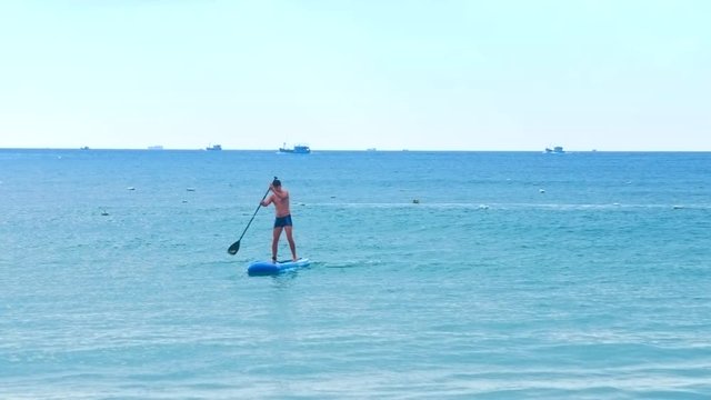pictorial view man trains to paddle standing on board in ocean against fishing motorboats on horizon under overcast sky