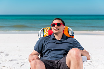 Happy man smiling face closeup lying on beach lounge chair during sunny day with red sunglasses in...