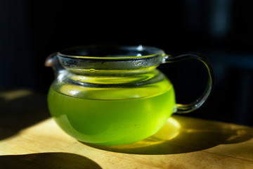 Closeup of glass teapot on wooden table in dark room with sunlight from window, filled with...