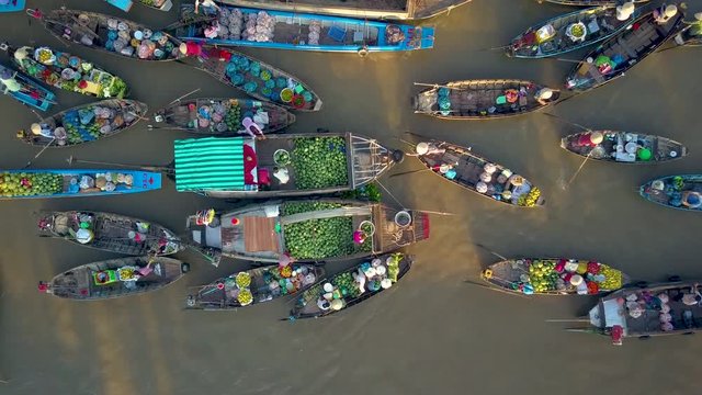 DRONE, TOP DOWN: Flying above local people doing business on the colorful floating market set on the calm murky river in the scenic Vietnamese countryside. People doing business on their wooden boats.