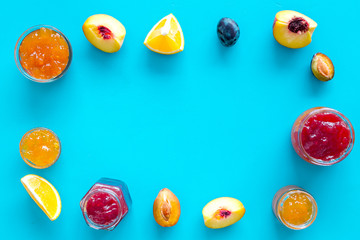 Jams different tastes made of fruits and berries near pieces of fruits on blue background top view frame