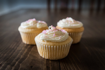 Three cupcakes on a wooden table surface. Sprinkled with pink crystals. Celebration.
