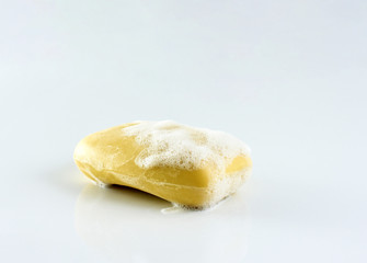 Yellow soap bar with bubble foam on white background.