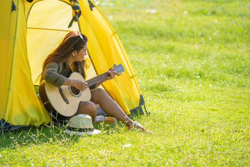 Beautiful women camping and playing a guitar surround with fresh air on sunny day. Women having a holiday alone in countryside.