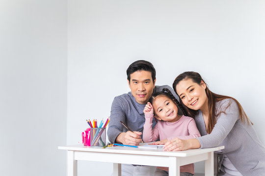 Asian family girl kid, mother and father doing drawing with many colour pencils on white paper over white background