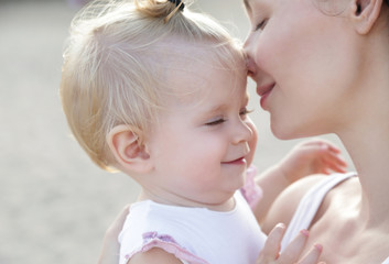 
Outdoor portrait of young mother holding an adorable baby girl, natural light candid shoot