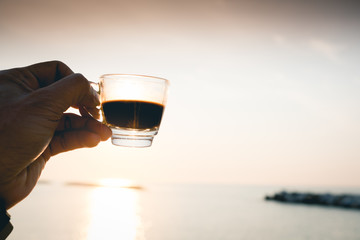 Closeup hand hold coffee cup on sand beach and view of sunset or sunrise background