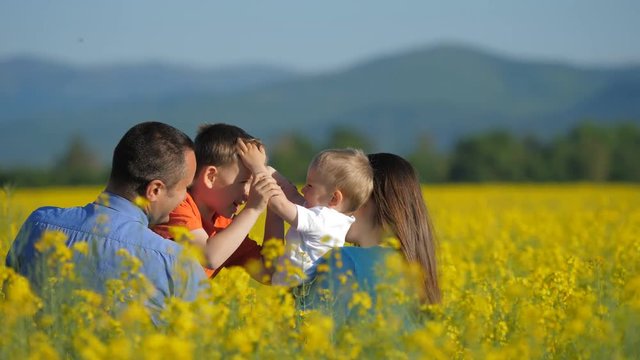 Happy family in blossom rape field, children play, kiss and embrace, smiling