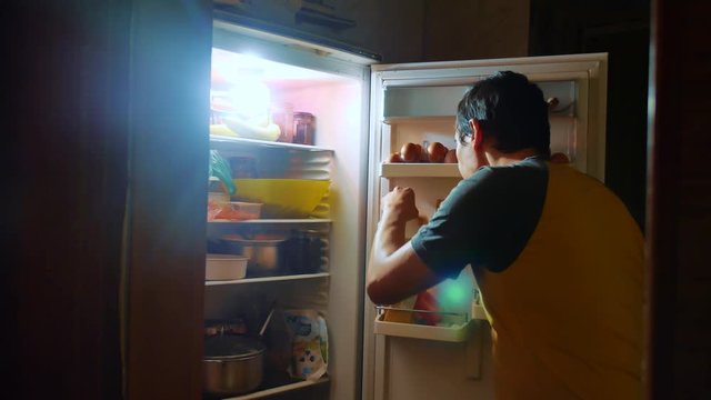 man eats hunger and gluttony from the refrigerator at night. man looks into the fridge at night. lifestyle gluttony overweight overeating concept