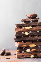 Chocolate tower. Dark and milk chocolate bars with nuts, berries and coffee beans on a grey background