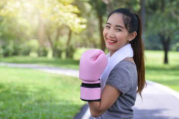 Cute young fitness girl in pink boxing gloves in park, smiling with camera