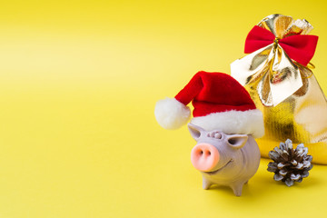 Christmas new year concept. The figure of the pig in the Santa hat cones gifts on a yellow background. Copy space