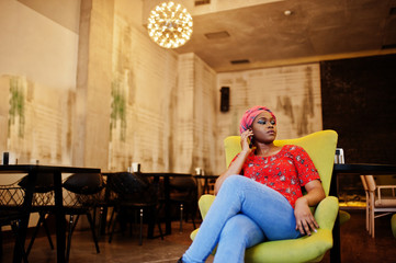 Obraz premium Stylish african woman in red shirt and hat posed indoor cafe and speaking mobile phone.