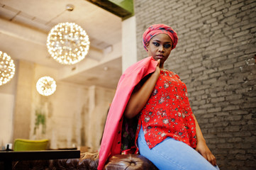 Stylish african woman in red shirt, jacket and hat posed indoor cafe.