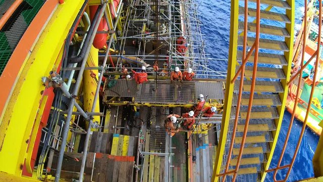 Top view of time lapse offshore workers with personal protective equipment (PPE)  performing construction activities on oil and gas platform. 