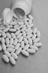Medicine tablets or pills spilled from fallen pill bottle on gray background. Pharmacy and healthcare concept.