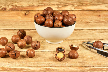 Macadamia nuts in the white bowl and nutcracker on wooden table, close-up