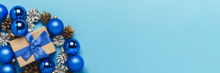 Gift box with blue ribbon, Christmas-tree decorations, balls and white and gold pine cones on a blue background. Concept of Merry Christmas and Happy New Year. Minimalism. Flat lay, top view. Banner