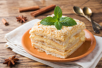 Layered cake with cream Napoleon millefeuille vanilla slice with mint on wooden background.