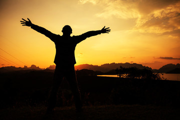 Man with arms raised and sunset.