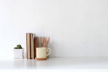 Workspace coffee mug, books, pencil and cactus on white desk.