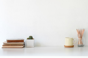 Workspace coffee mug, books, pencil and cactus on white desk.
