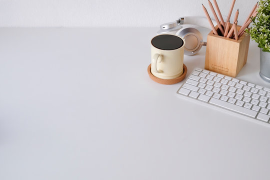 Office desk coffee mug, computer keyboard, pencil and headphone on table.